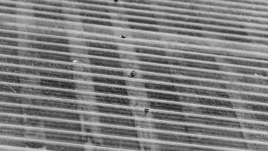 Close-up of a grey corrugated cement sheet roof with fixing bolts through the crowns, the profile typical of asbestos garage roofs in Carlisle