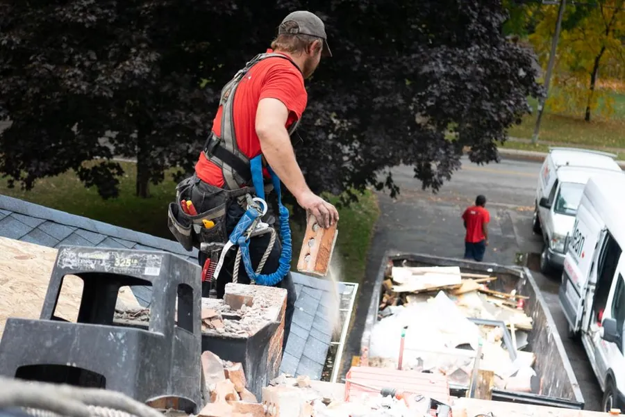 A worker in a safety harness stripping roof material into a container below, the controlled removal an asbestos garage roof requires