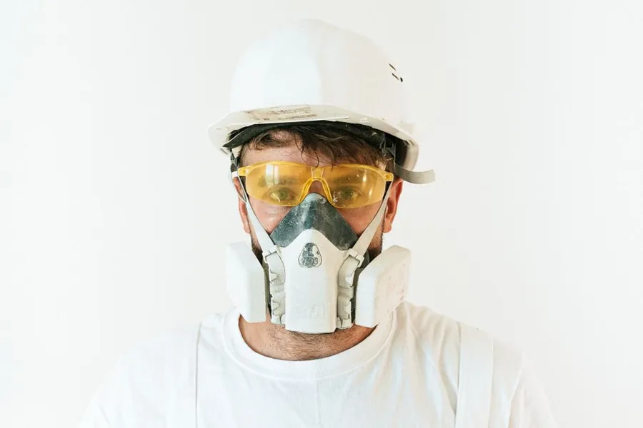 A worker in a hard hat, goggles and respirator mask, the protective equipment required for handling asbestos cement sheet