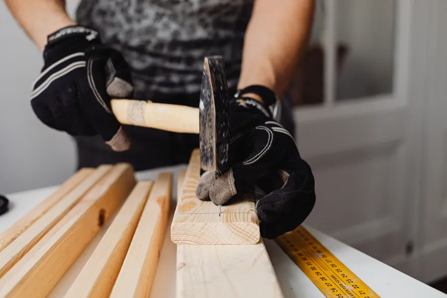 Gloved hands nailing a softwood batten, the fixing work that creates the drained cavity above a sarked roof deck