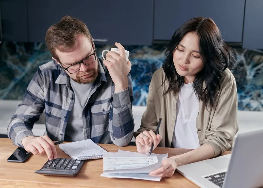 A couple working through household bills and a calculator at a kitchen table, budgeting for a new roof in Carlisle