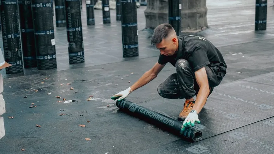 A worker laying waterproof membrane across a roof deck, one of the hidden layers included in a Carlisle re-roofing quote