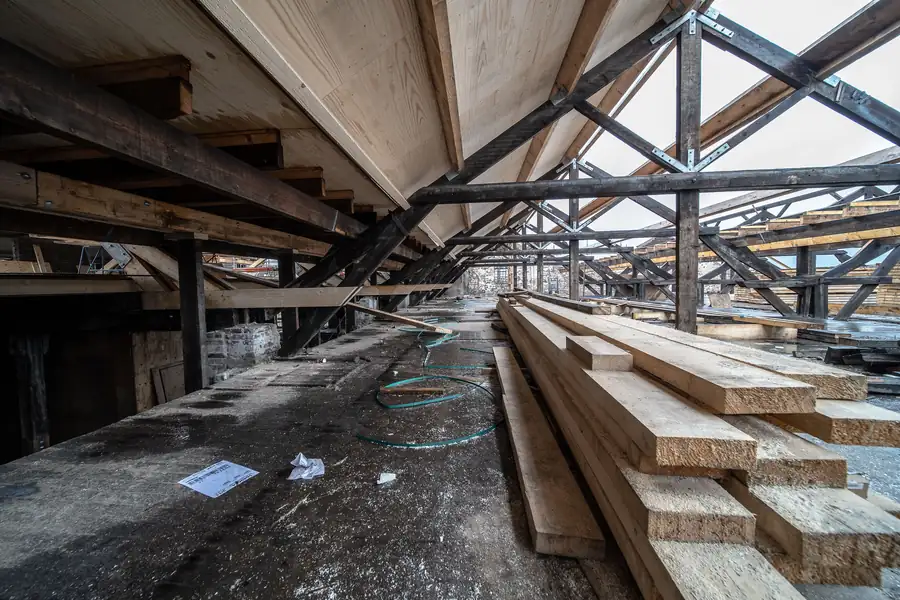 New timber stacked in an open roof space alongside old blackened beams during re-boarding work on a Carlisle roof