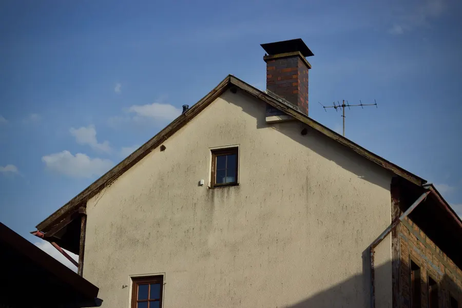 Weathered, decaying bargeboards along the sloping edge of a rendered gable end, exposed to the prevailing weather