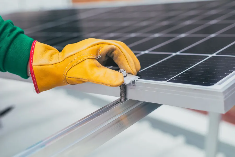A gloved hand tightening the clamp that fixes a solar panel to its mounting rail, the fixing work behind every argument over who pays for a Carlisle roof leak