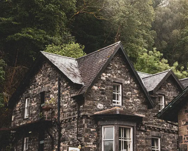 Rain-soaked solid stone wall and slate roof on an older Cumbrian property near Carlisle