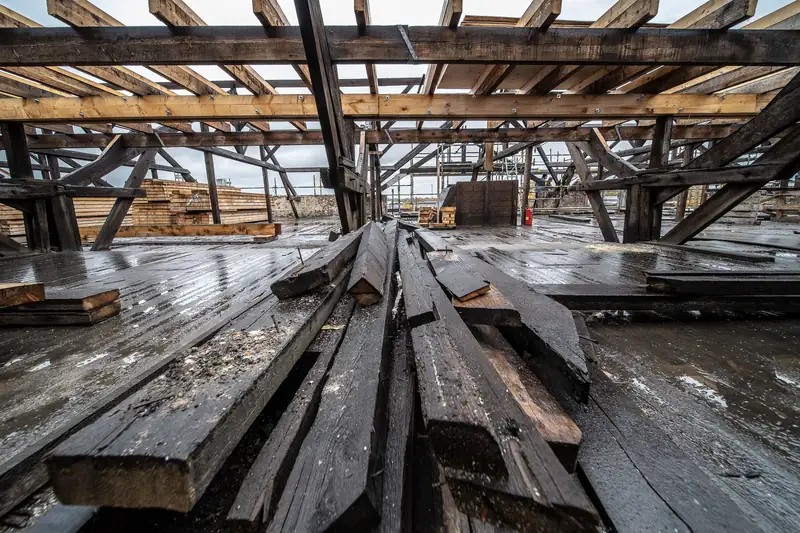 A roof stripped back to wet, blackened timbers with boards and offcuts stacked, the messy middle stage of a Carlisle re-roof