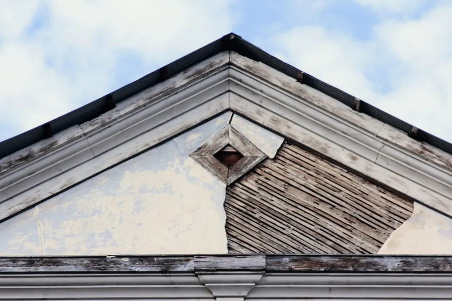 Weathered timber boards at a roof edge with the paint worn away and the grain split, the sort of rot uPVC capping gets fitted over