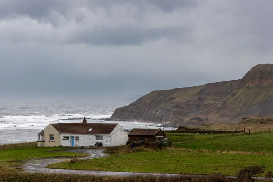 Exposed house on the Cumbrian coast under a dark sky, the conditions that produce wind-driven rain near Carlisle