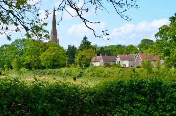 An English village scene of cottages and a church spire across green space, the character Dalston's green gives it