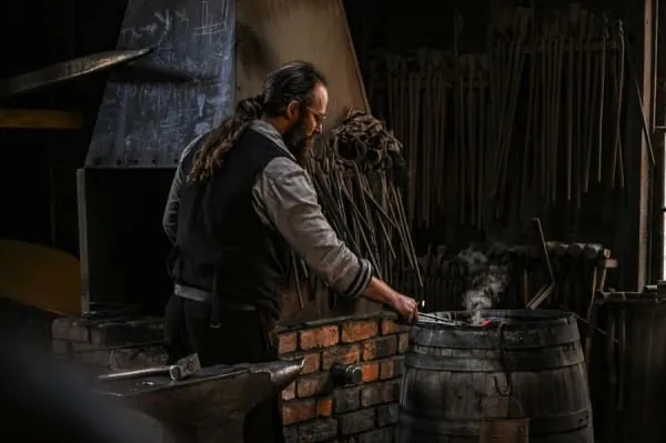 A blacksmith working at an anvil in a dark forge, the craft the Famous Blacksmiths Shop is built around