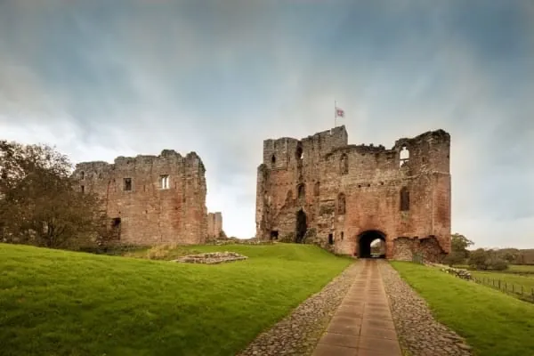 Red sandstone castle ruins on a grass mound, as at Penrith Castle park