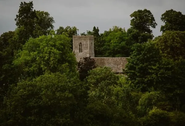 A stone parish church tower rising among trees, in the manner of St Mary's at Wigton