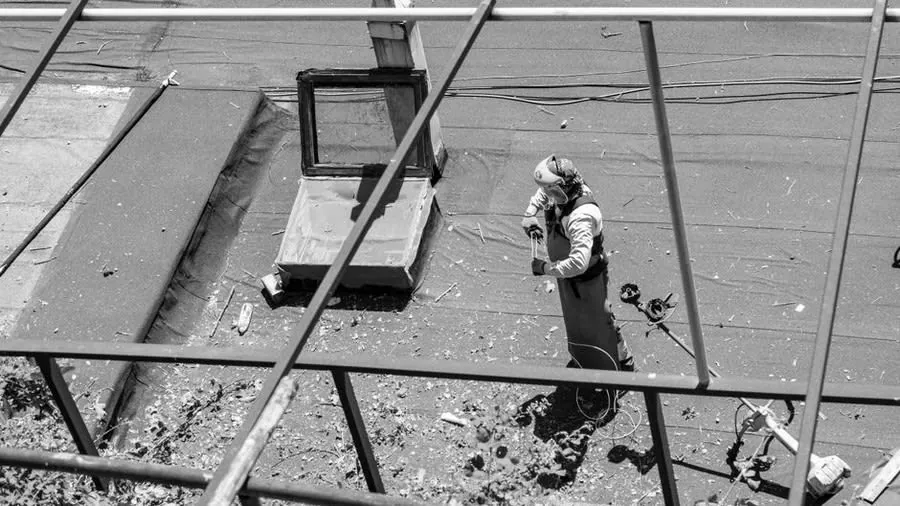 Roofer at work on an aged felt flat roof beside a rooflight upstand