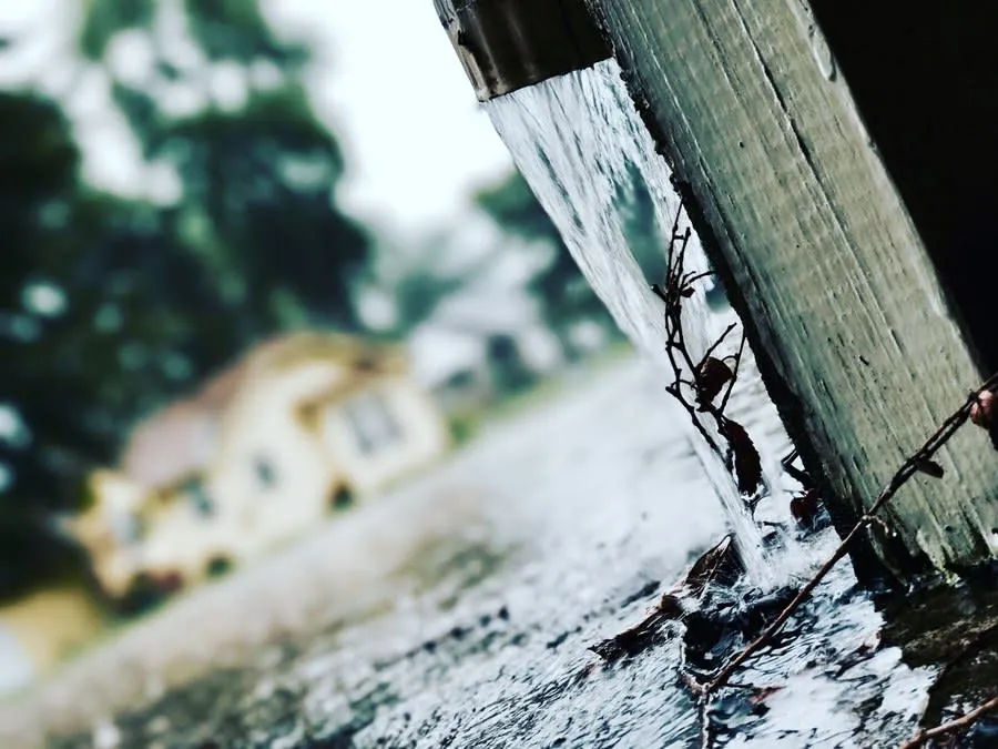 Rainwater pouring over the lip of a gutter during heavy rain, the pattern of a capacity problem rather than a blockage