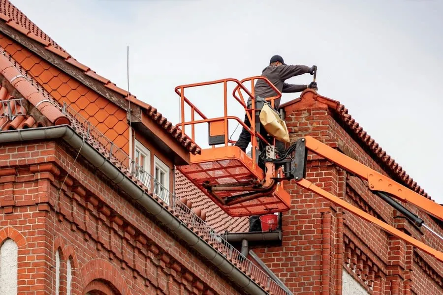 A roofer working at gutter level on a red brick house with a tiled roof