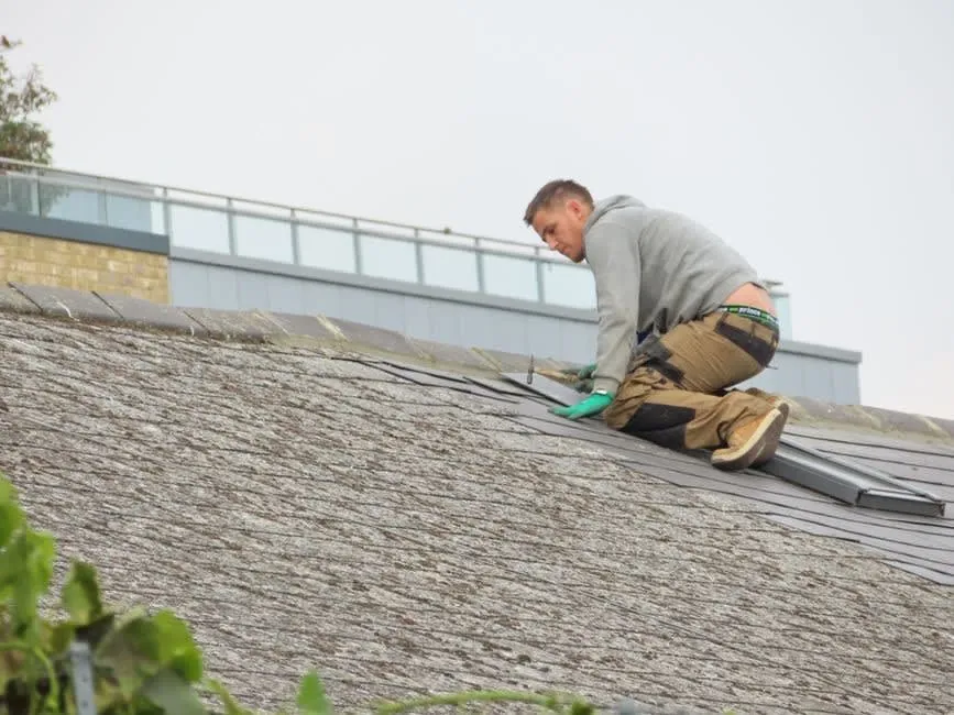 Roofer kneeling on a weathered roof to carry out a localised repair