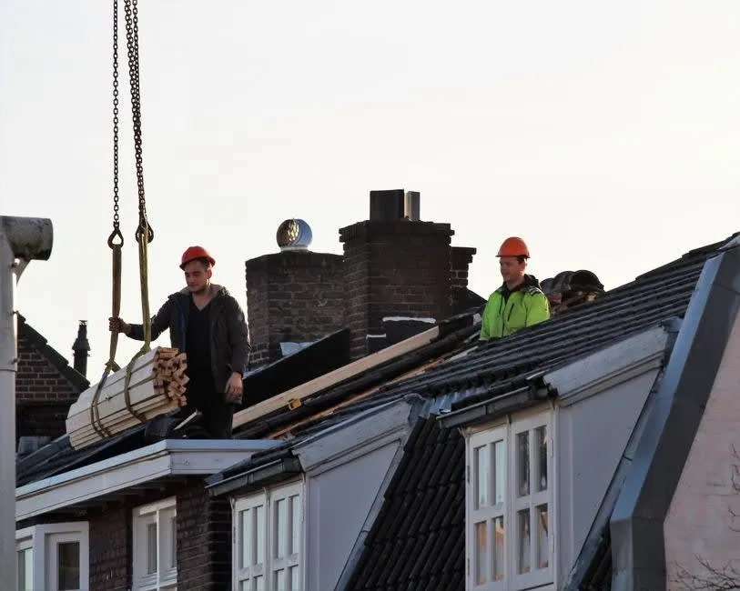 Roofers working at a chimney stack with materials being lifted to roof level in Carlisle