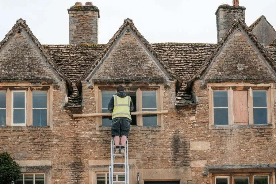 A tradesman up a ladder against a stone-built house, the kind of older stone property common in Brampton and Wetheral