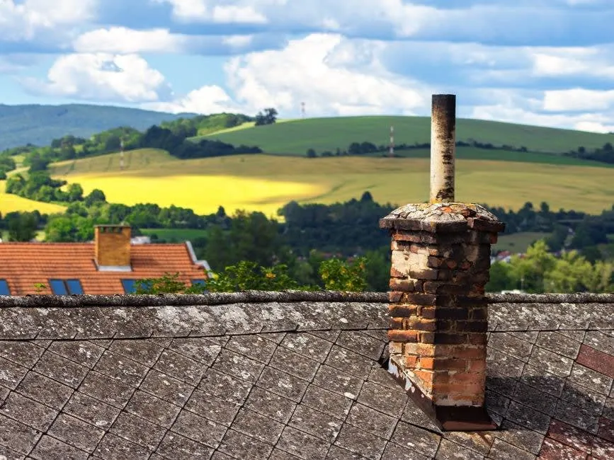 A weathered brick chimney stack standing above a roofline, the exposure a Carlisle stack lives with year round